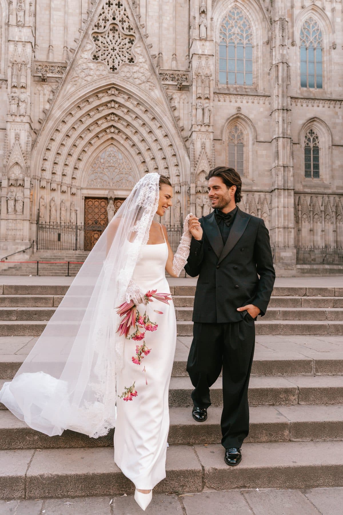 Bride laughing as she holds the groom's hand on the cathedral steps