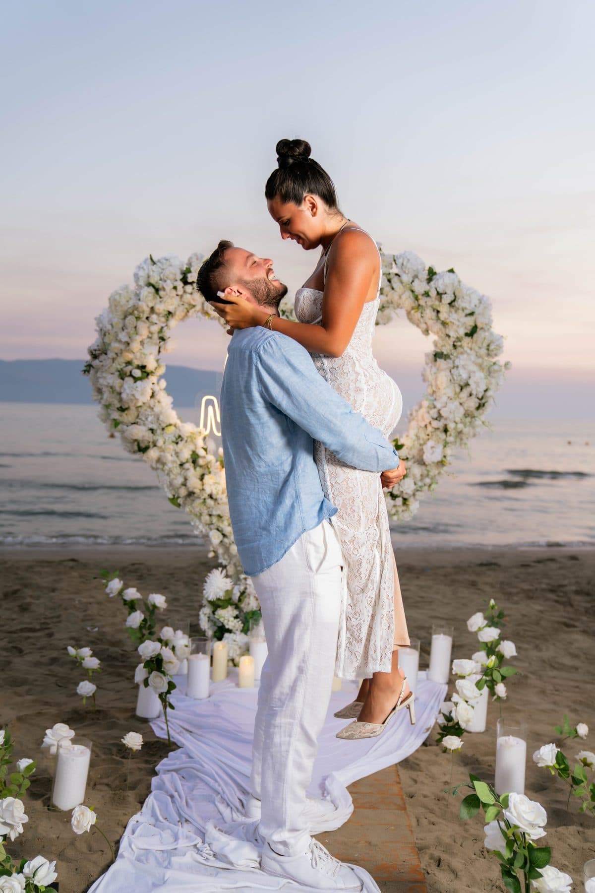Proposal on the beach in front of a heart of white flowers