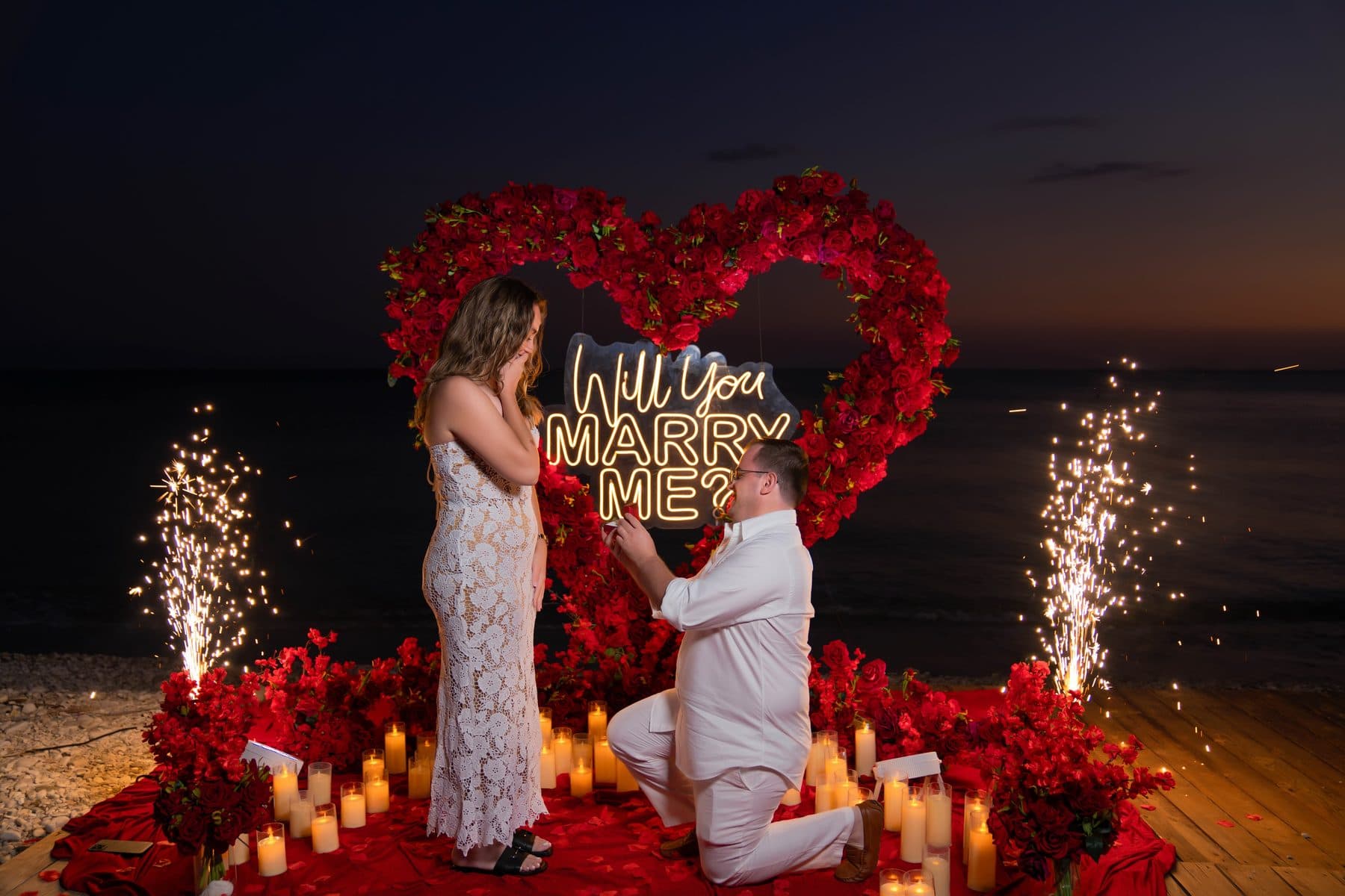 Proposal by the sea with a heart of red roses, candles and sparklers